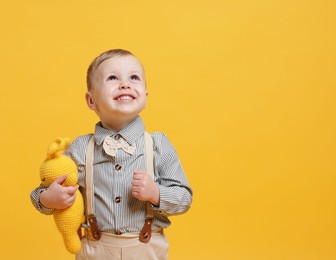 Photo of Cute little boy with toy bunny on yellow background. Space for text