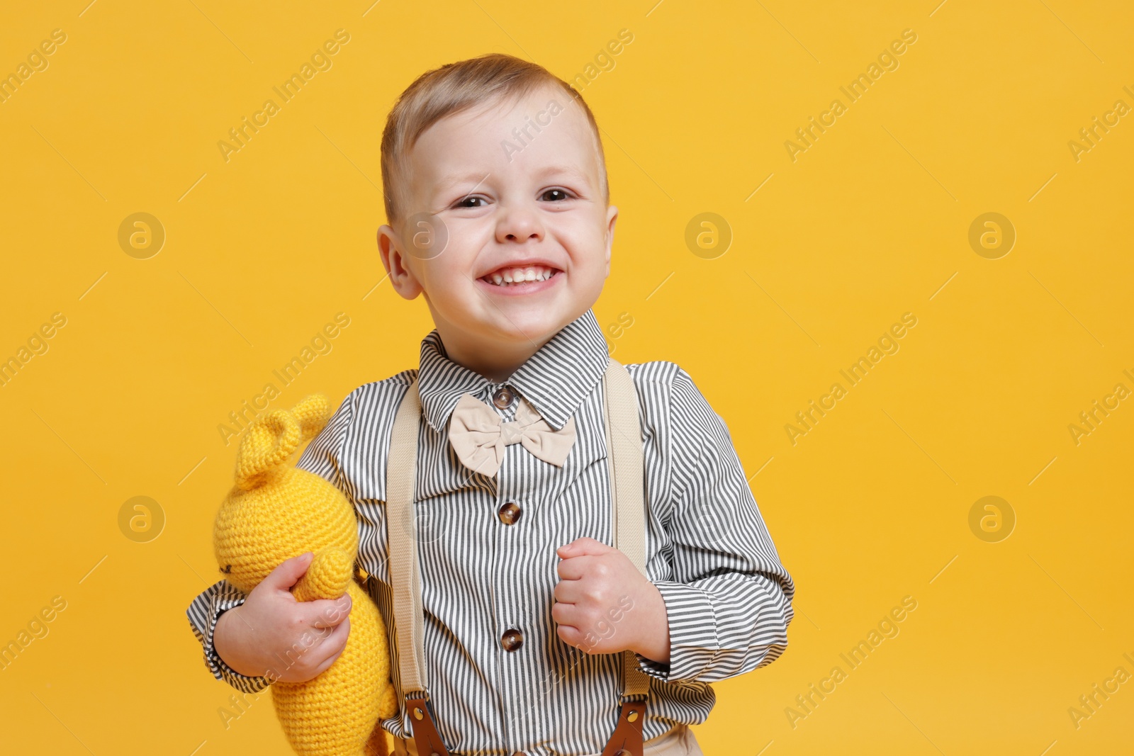 Photo of Cute little boy with toy bunny on yellow background