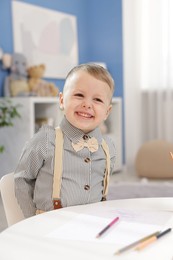 Photo of Little boy with colorful pencils at table indoors