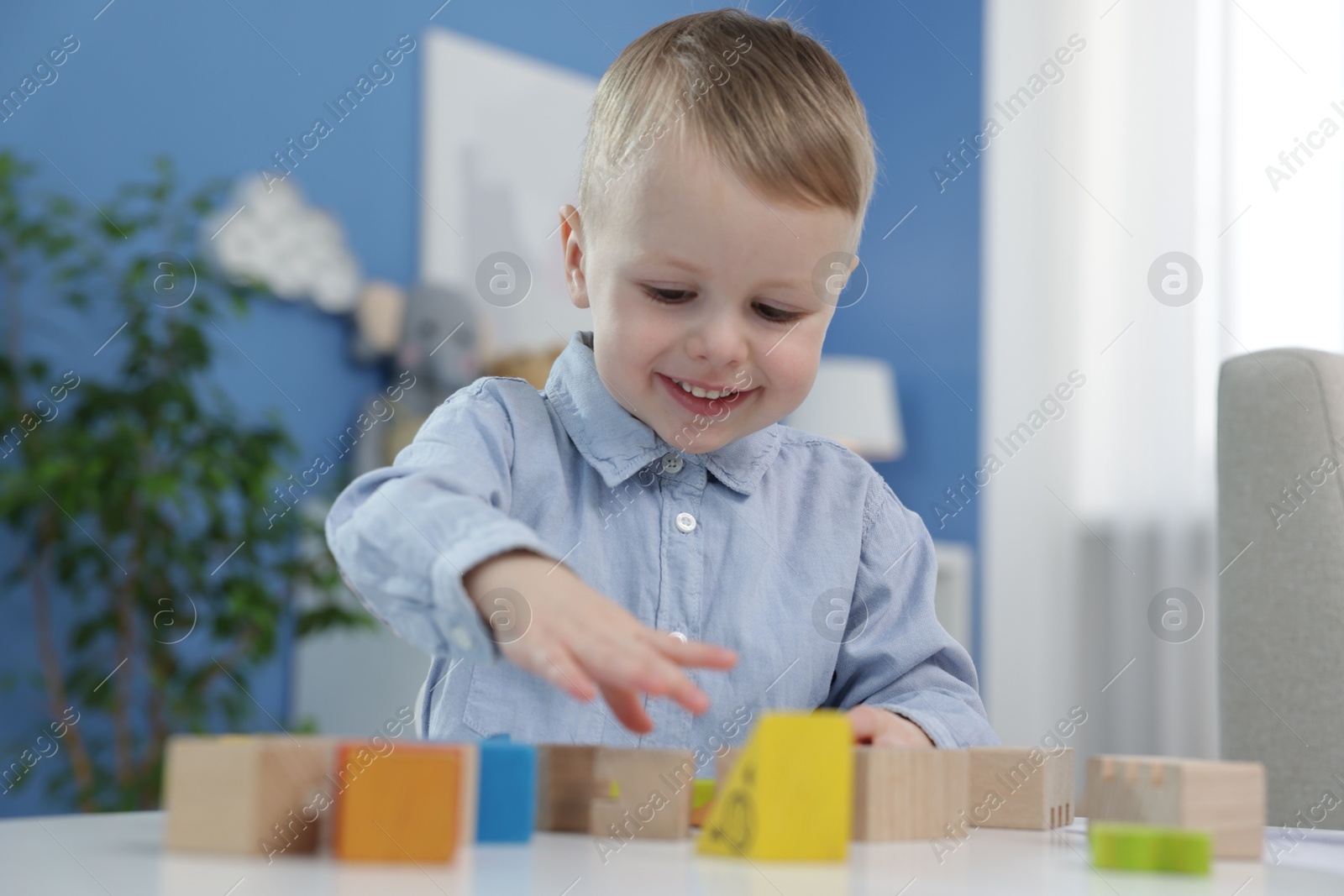 Photo of Little boy playing with wooden blocks at table indoors