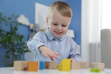 Photo of Little boy playing with wooden blocks at table indoors