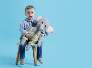 Photo of Cute little boy with toy elephant on light blue background. Space for text