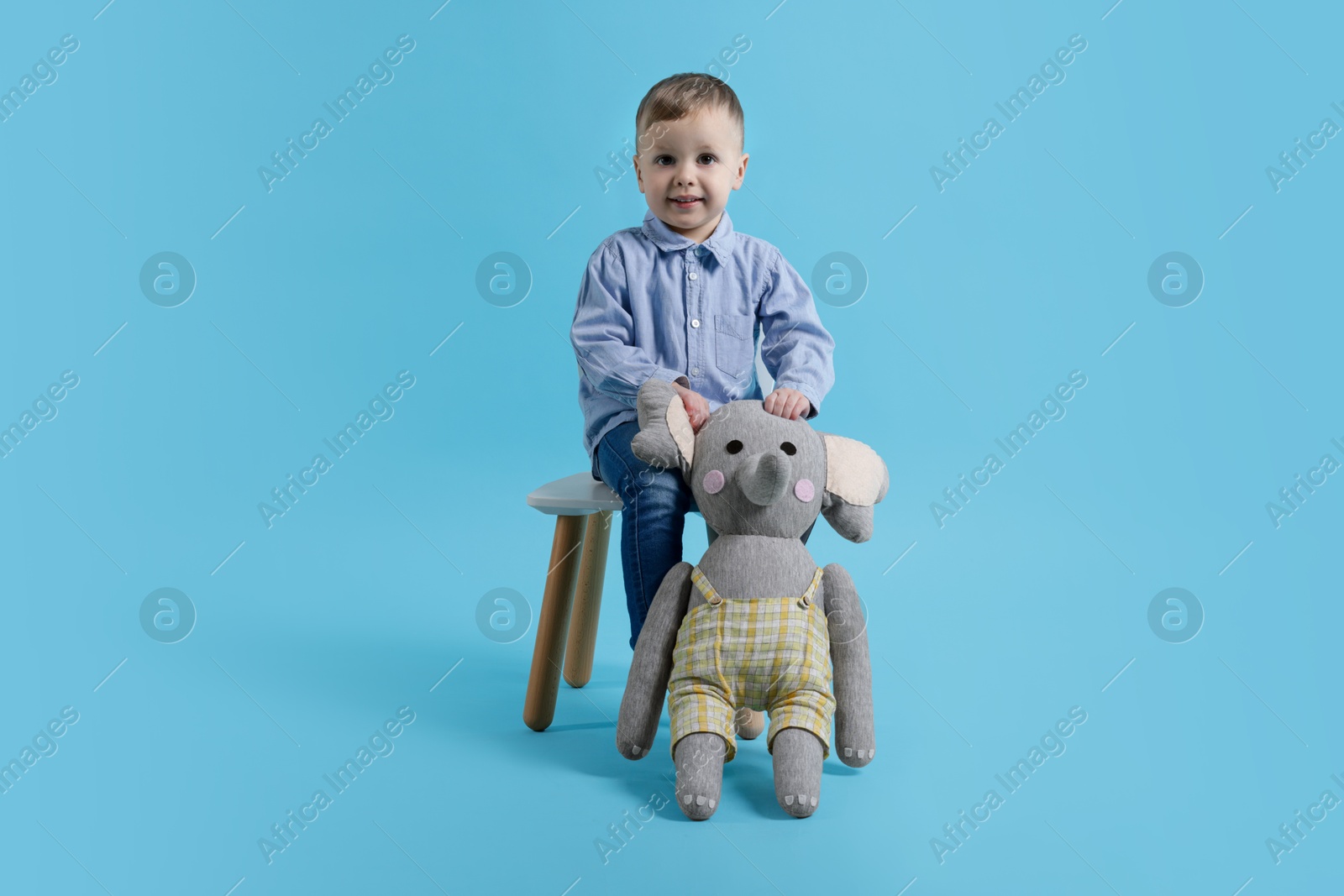 Photo of Cute little boy with toy elephant on light blue background