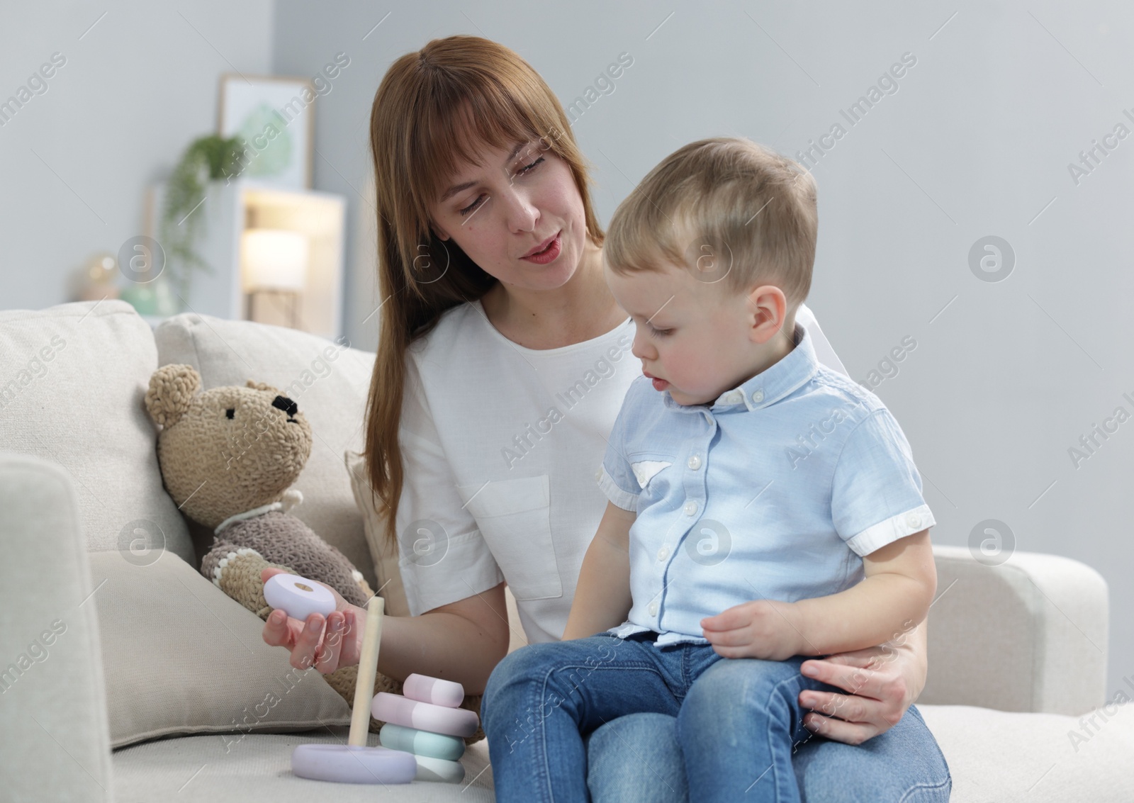 Photo of Mother and son playing with toy pyramid on sofa indoors