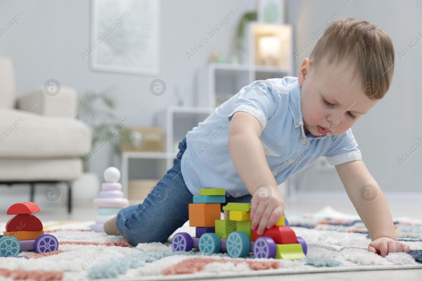 Photo of Little boy playing with toy train on floor indoors. Space for text