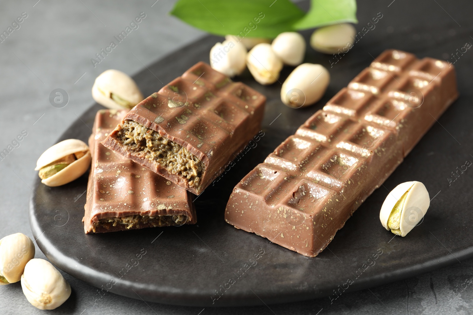 Photo of Delicious Dubai chocolate bars and pistachios on grey table, closeup