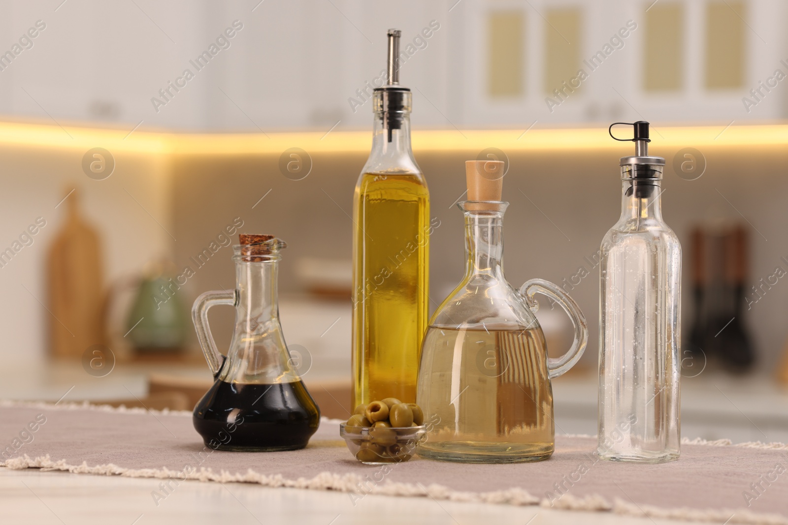 Photo of Bottles of salad dressings and olives on white table in kitchen