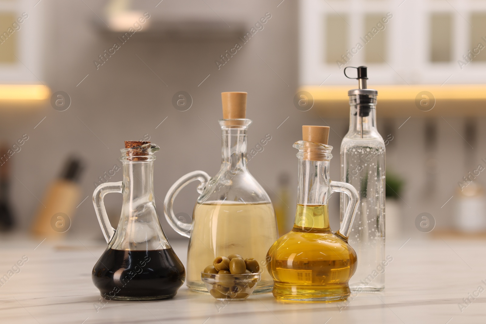 Photo of Bottles of salad dressings and olives on white table in kitchen