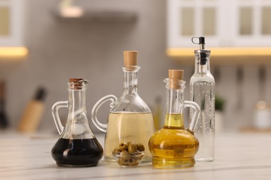 Photo of Bottles of salad dressings and olives on white table in kitchen