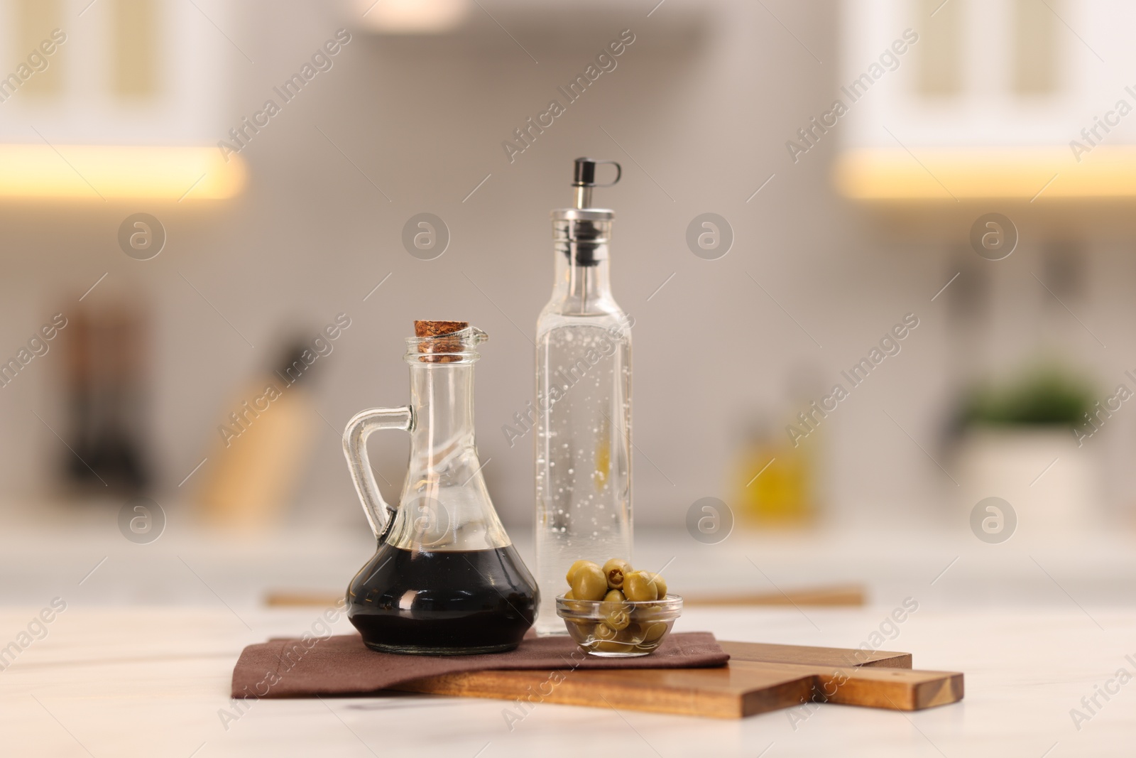 Photo of Bottles of salad dressings and olives on white table in kitchen