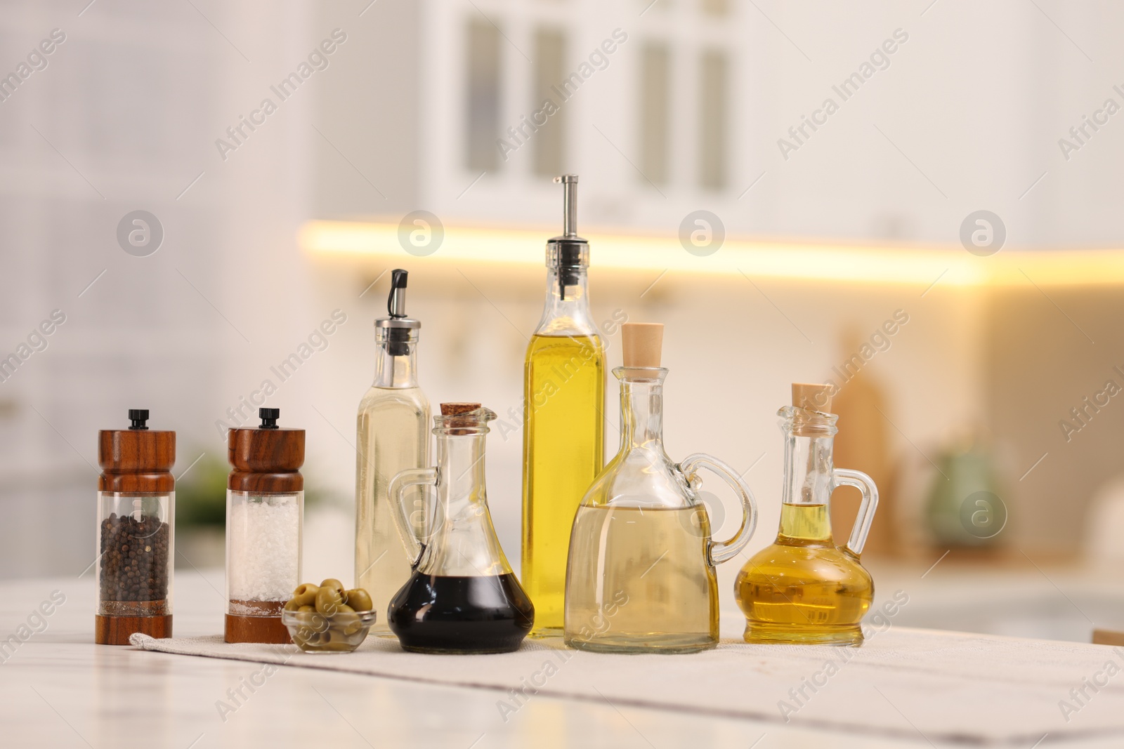 Photo of Bottles of salad dressings, salt, pepper and olives on white table in kitchen