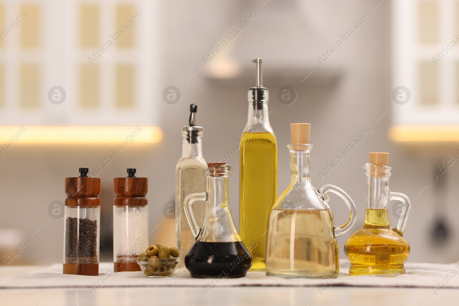 Photo of Bottles of salad dressings, salt, pepper and olives on white table in kitchen