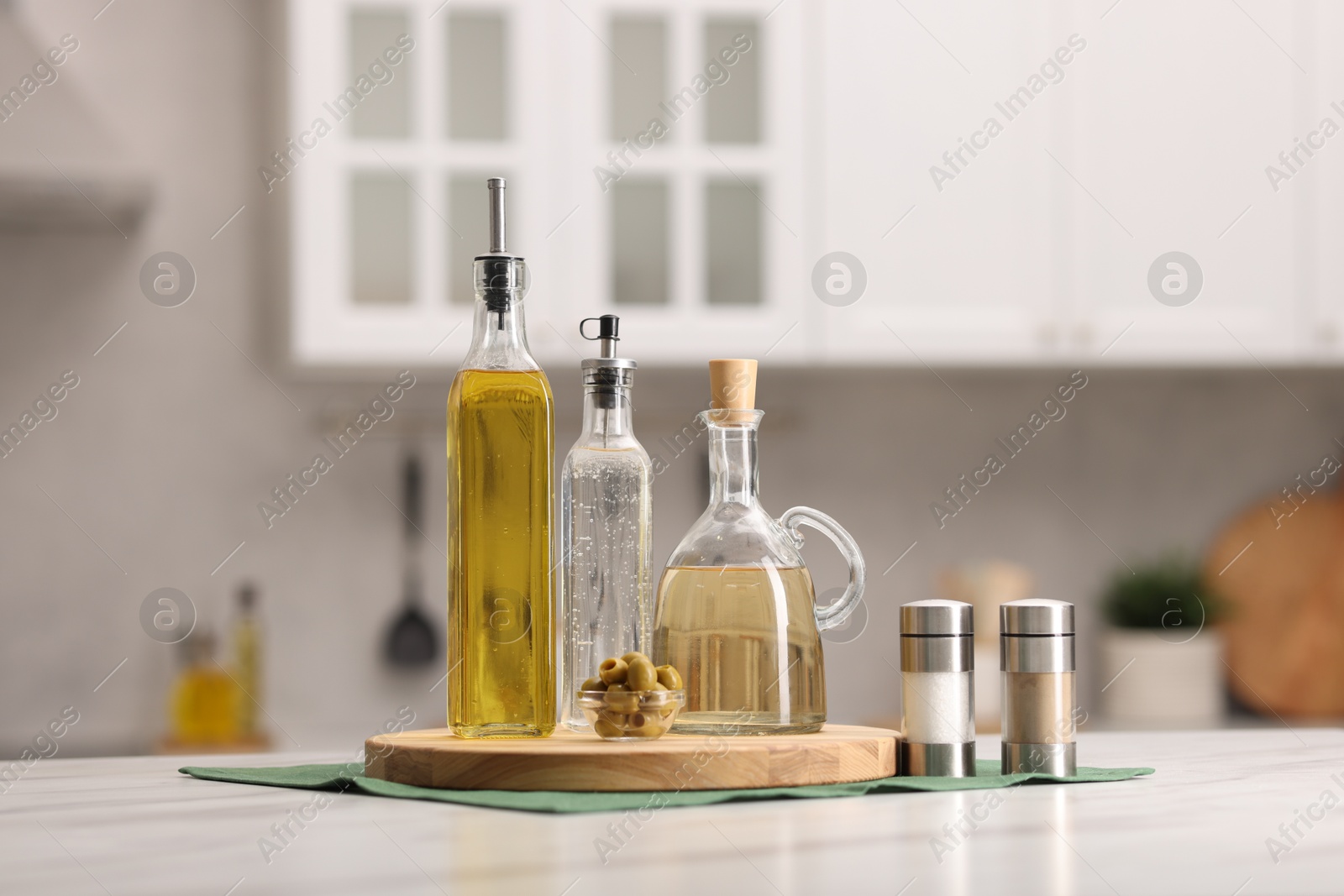 Photo of Bottles of salad dressings, salt, pepper and olives on white table in kitchen