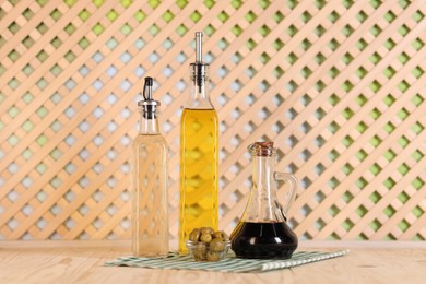 Photo of Bottles of salad dressings and olives on wooden table