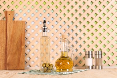 Photo of Bottles of salad dressings, salt, pepper and olives on wooden table