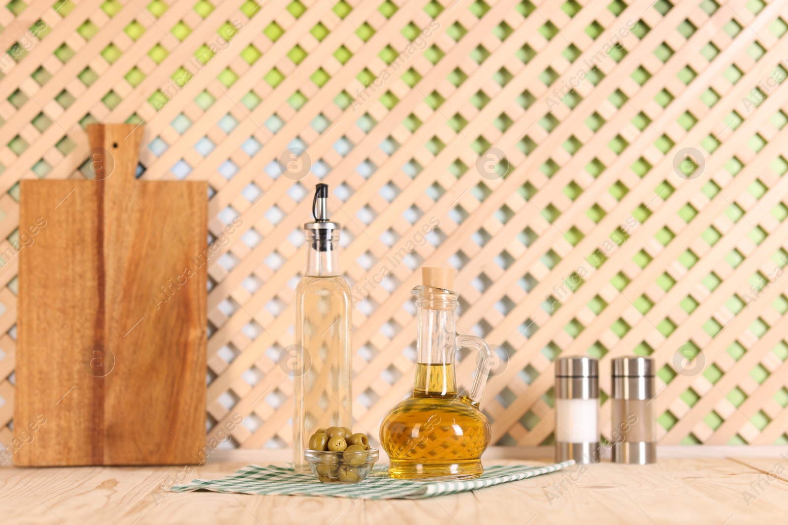 Photo of Bottles of salad dressings, salt, pepper and olives on wooden table