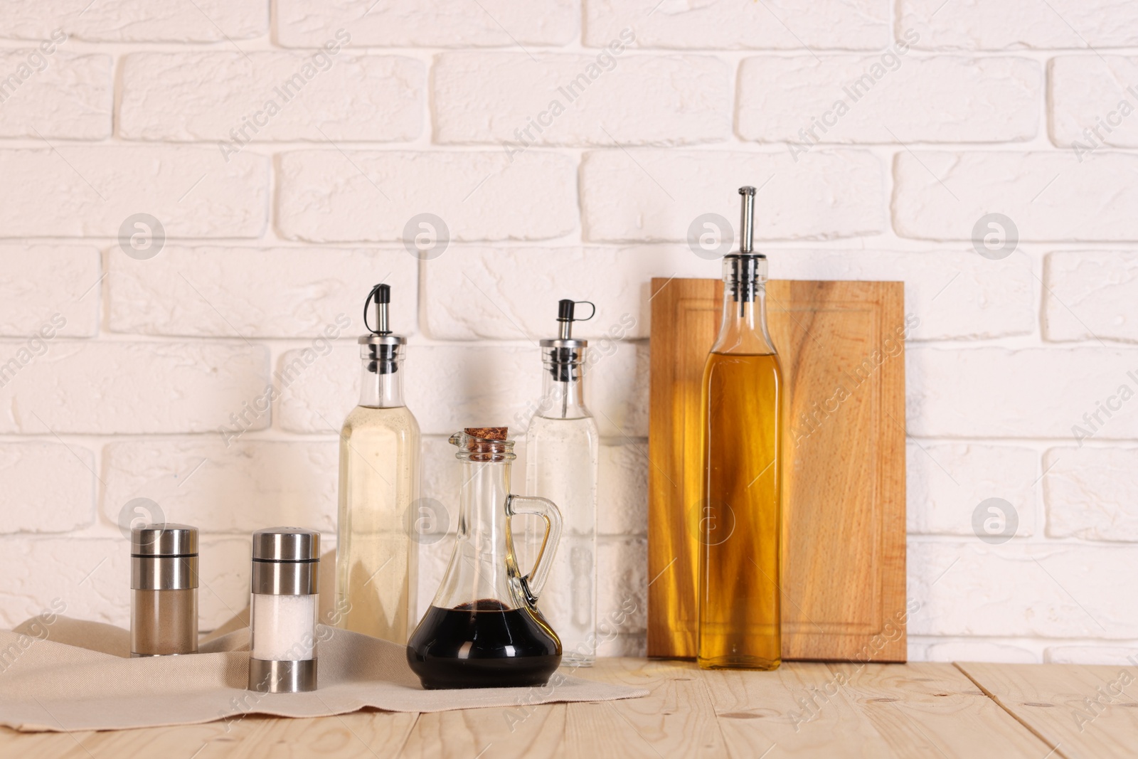 Photo of Bottles of salad dressings, spices and cutting board on wooden table