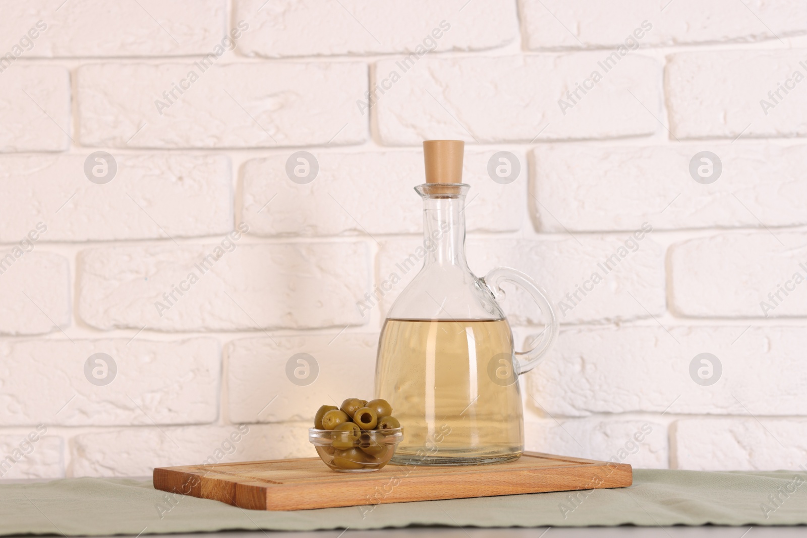 Photo of Bottle of salad dressing and olives on table near white brick wall