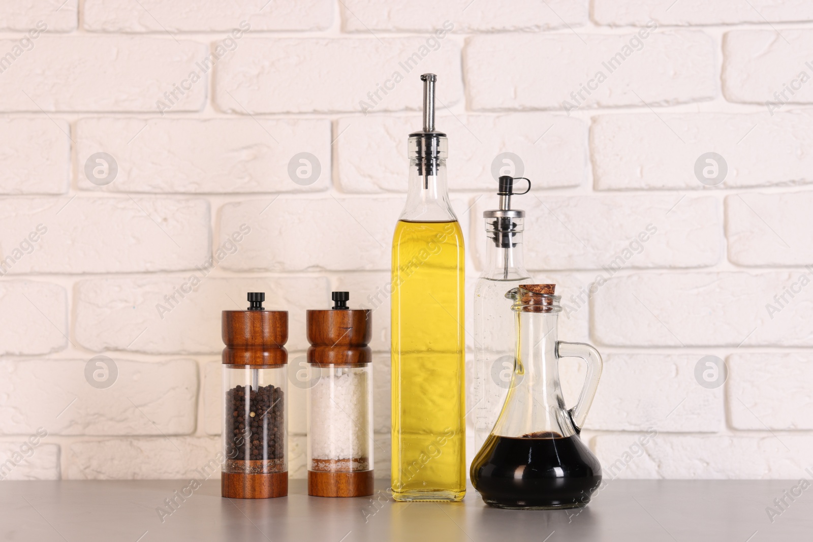 Photo of Bottles of salad dressings, salt and pepper on white table near brick wall