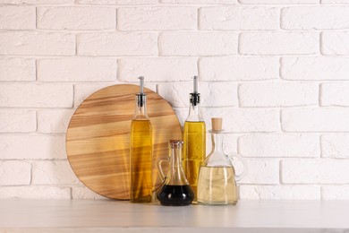 Photo of Bottles of salad dressings and cutting board on white table near brick wall