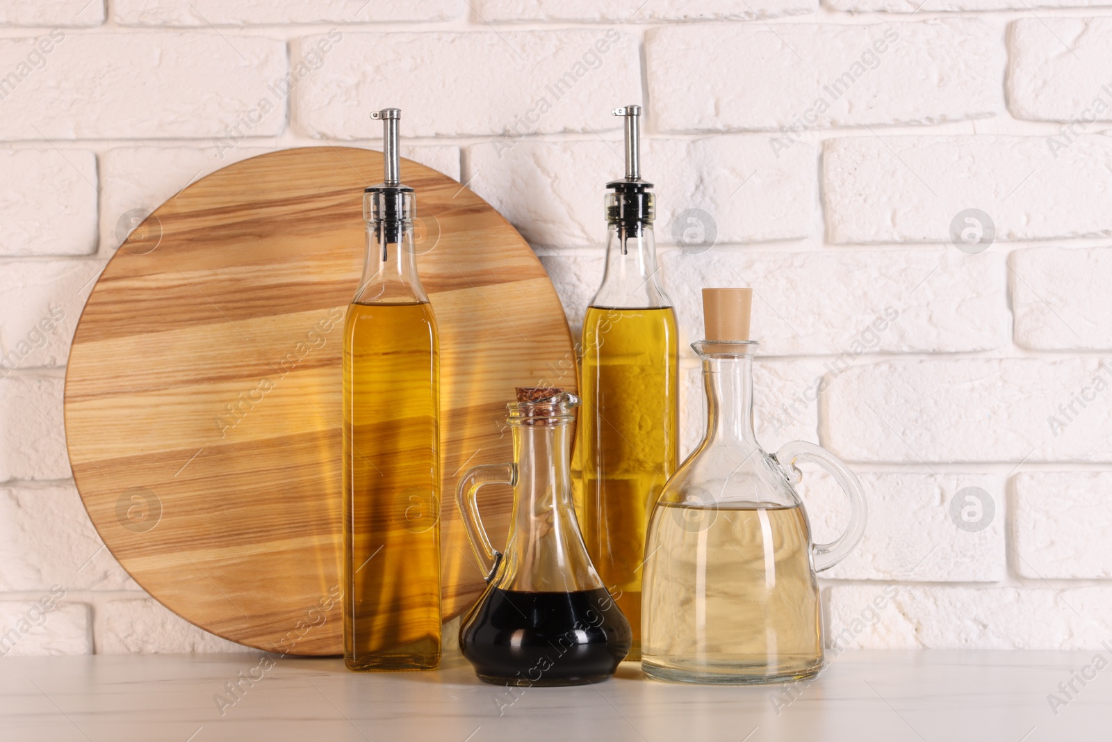 Photo of Bottles of salad dressings and cutting board on white table near brick wall