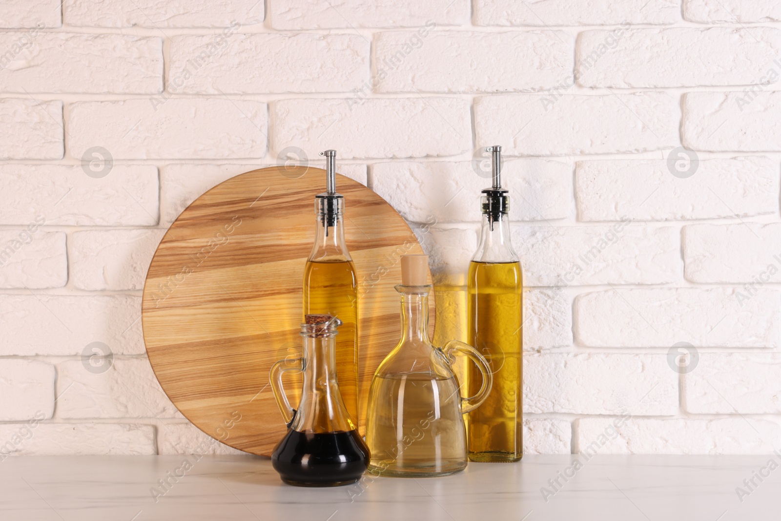 Photo of Bottles of salad dressings and cutting board on white table near brick wall