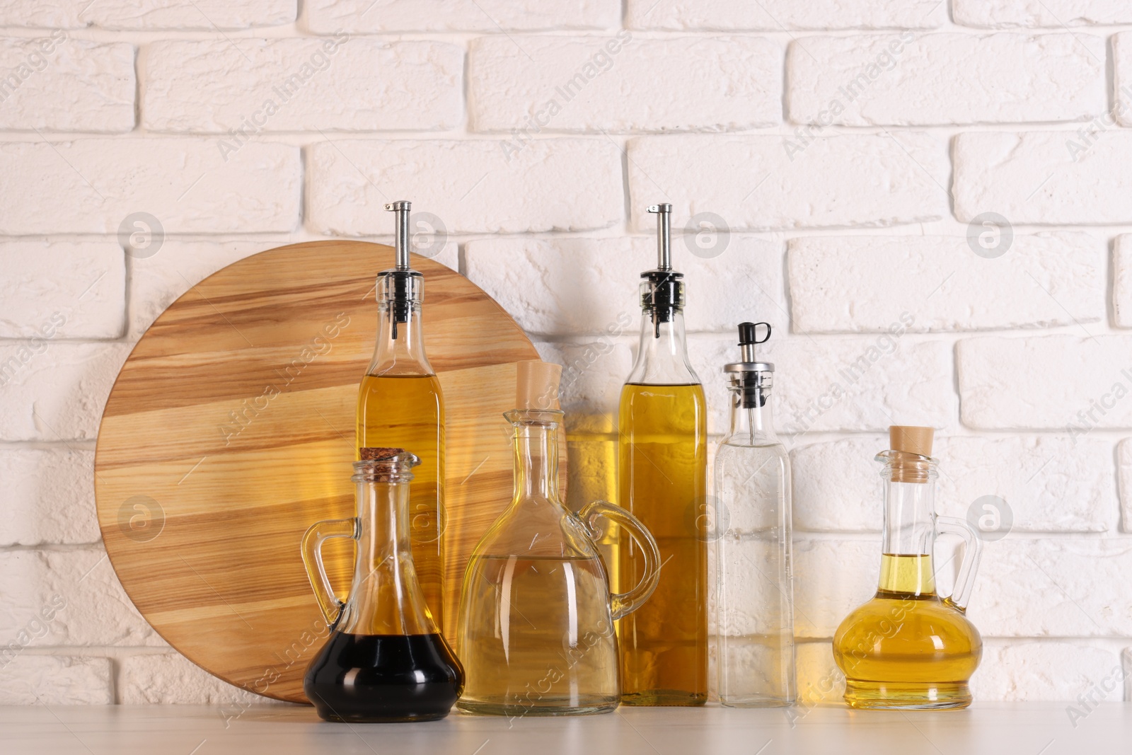 Photo of Bottles of salad dressings and cutting board on white table near brick wall