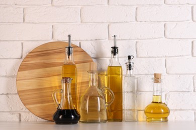 Photo of Bottles of salad dressings and cutting board on white table near brick wall