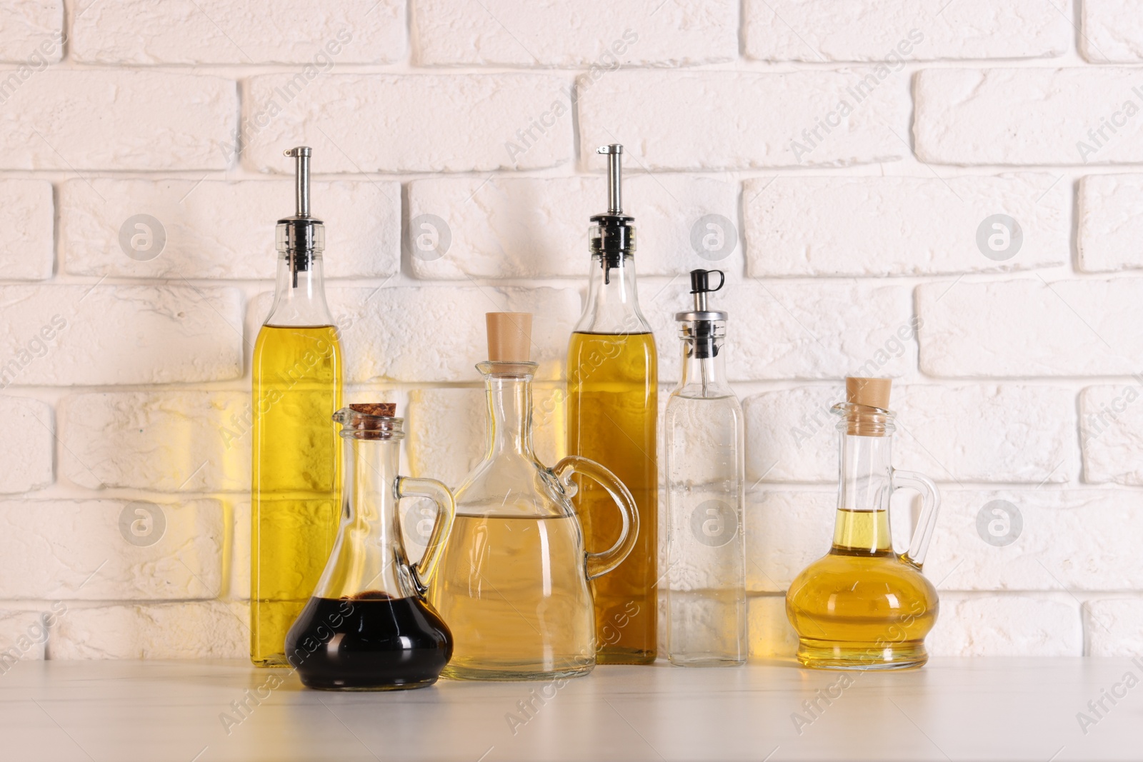 Photo of Bottles of salad dressings on white table near brick wall