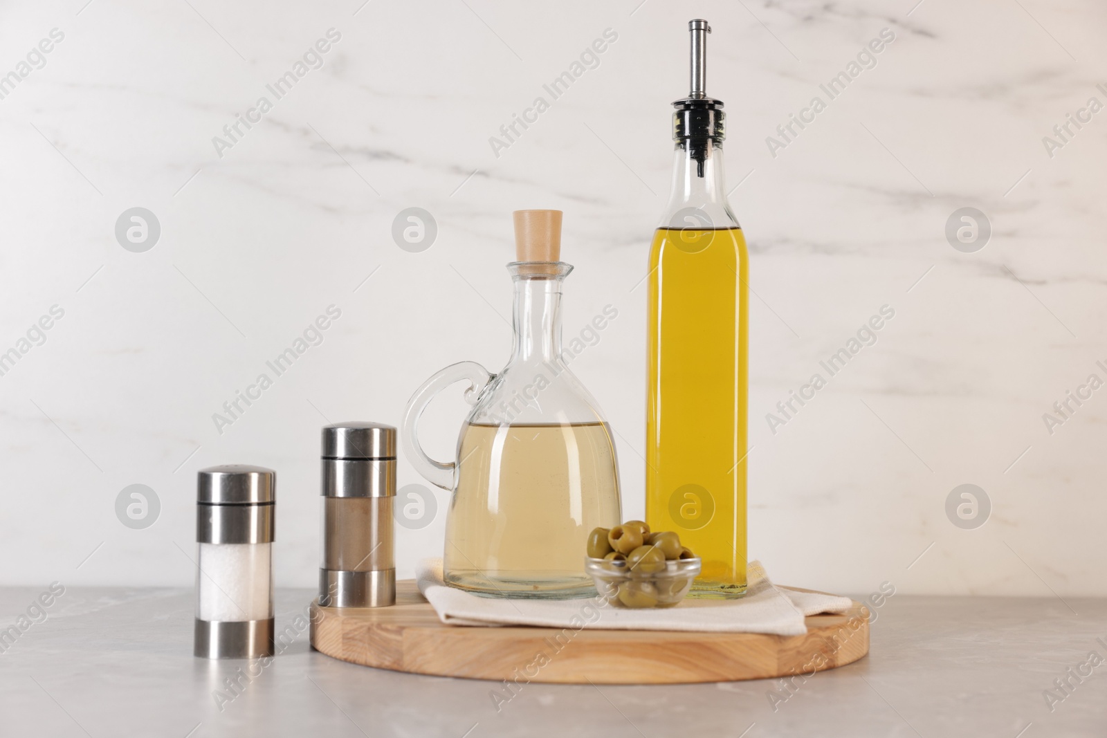 Photo of Bottles of salad dressings, salt, pepper and olives on light grey table