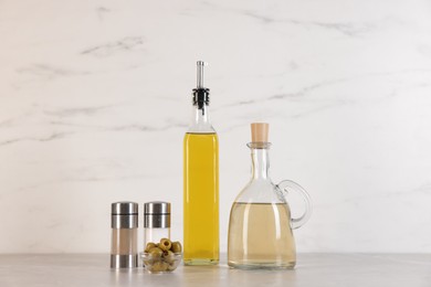 Photo of Bottles of salad dressings, salt, pepper and olives on light grey table