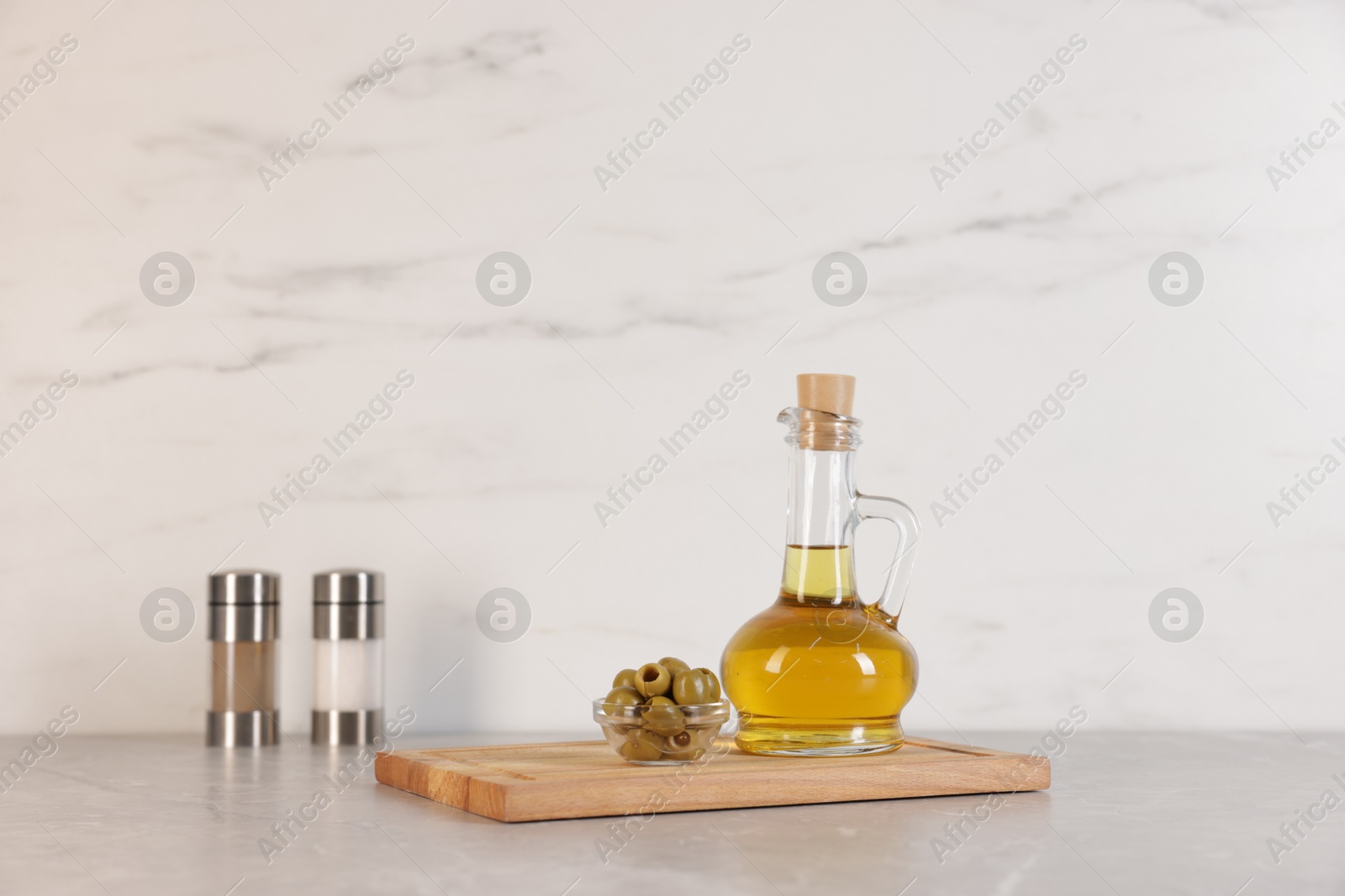 Photo of Bottle of oil, salt, pepper and olives on light grey table