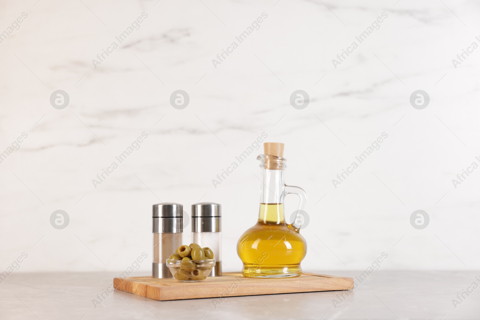 Photo of Bottle of oil, salt, pepper and olives on light grey table