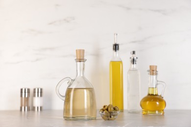 Photo of Bottles of salad dressings, salt, pepper and olives on light grey table