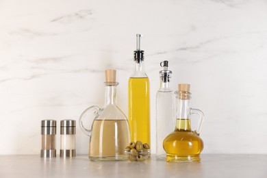 Photo of Bottles of salad dressings, salt, pepper and olives on light grey table