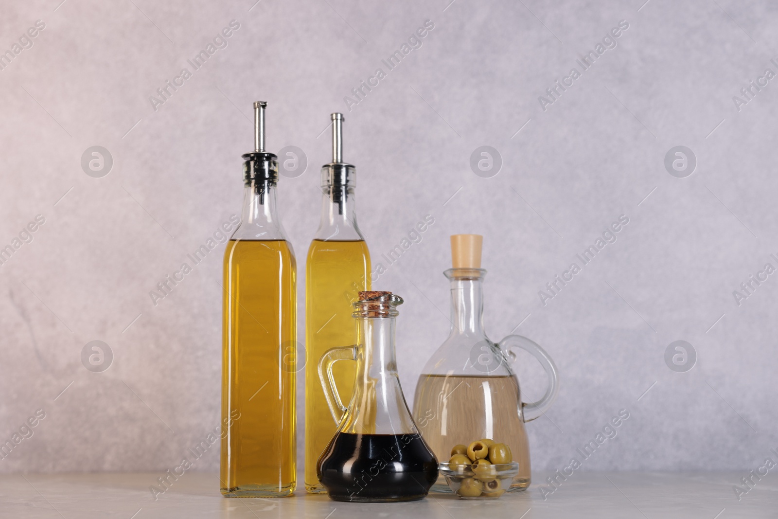 Photo of Bottles of salad dressings and olives on light grey table