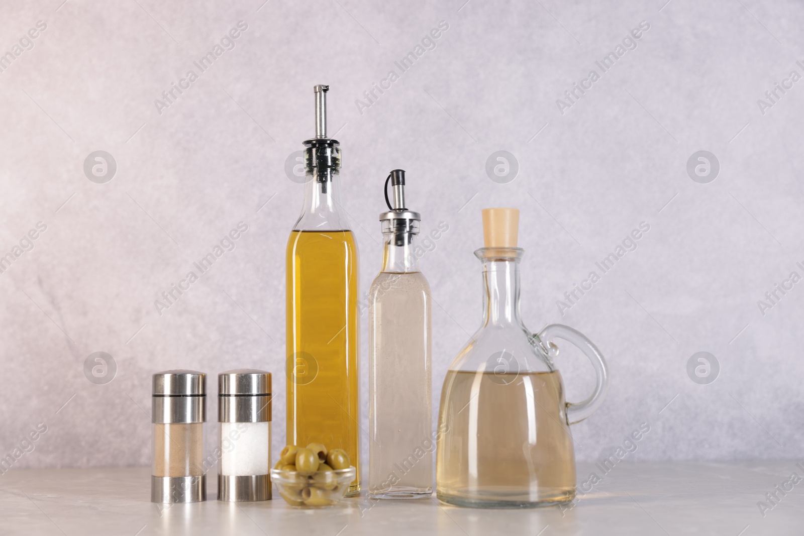 Photo of Bottles of salad dressings, salt, pepper and olives on light grey table