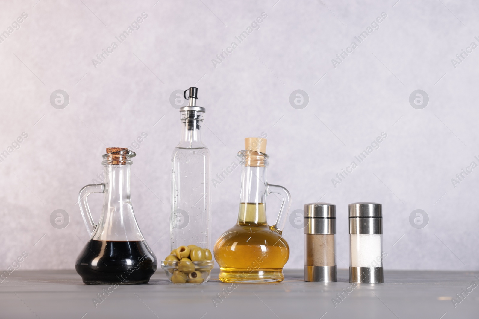 Photo of Bottles of salad dressings, salt, pepper and olives on light grey wooden table