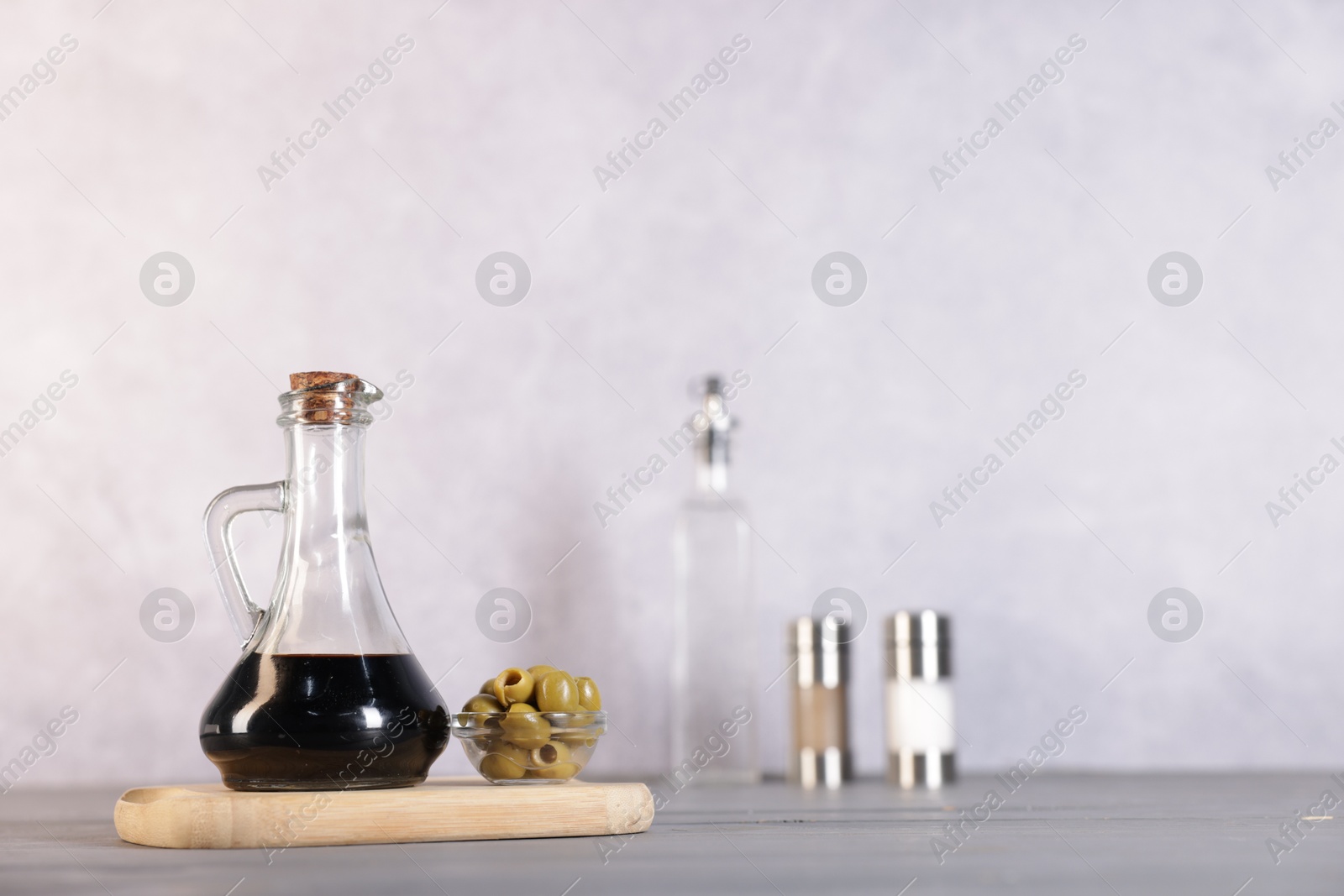 Photo of Bottle of balsamic vinegar and olives on light grey wooden table