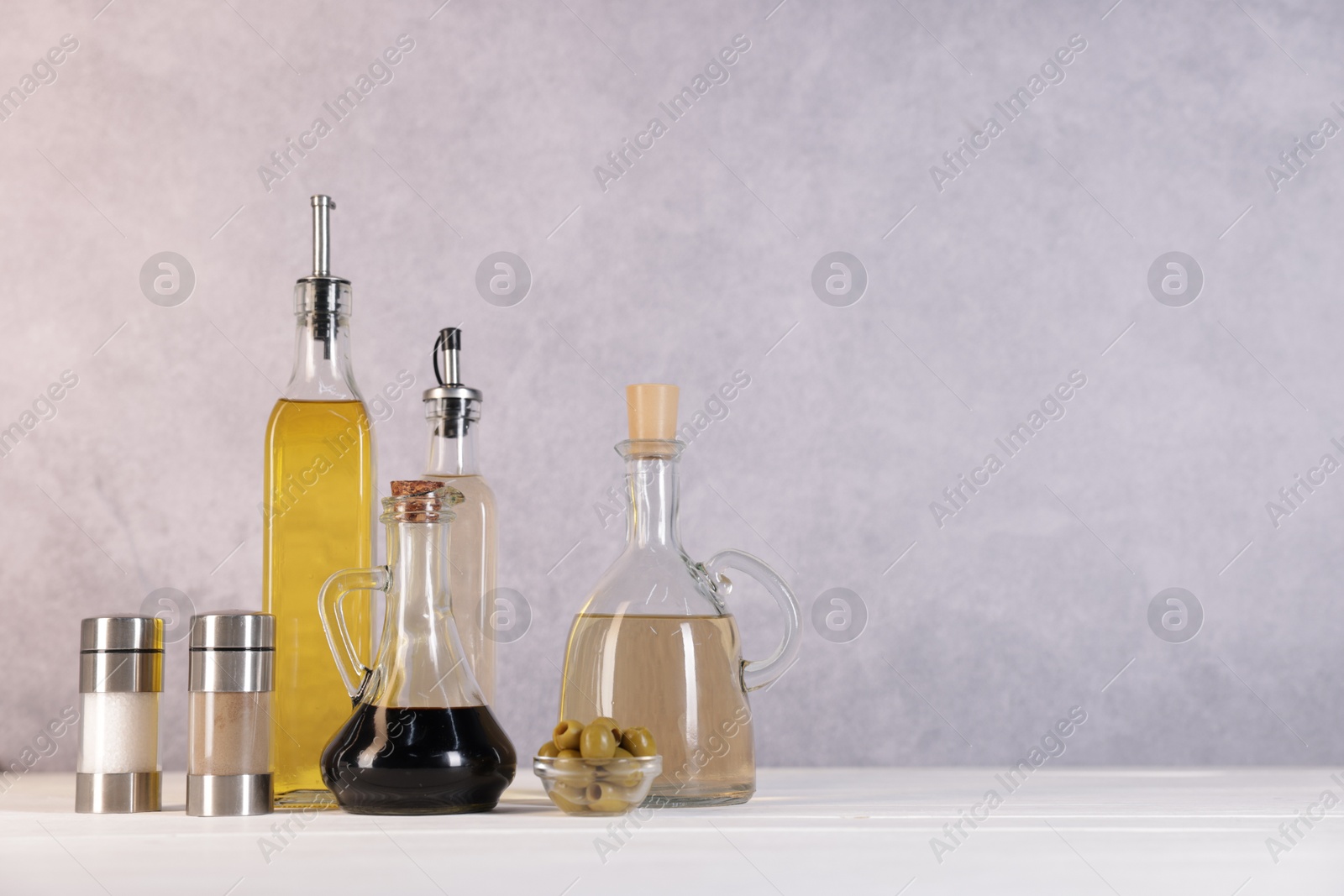 Photo of Bottles of salad dressings, salt, pepper and olives on white wooden table, space for text