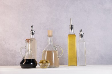 Photo of Bottles of salad dressings and olives on white wooden table