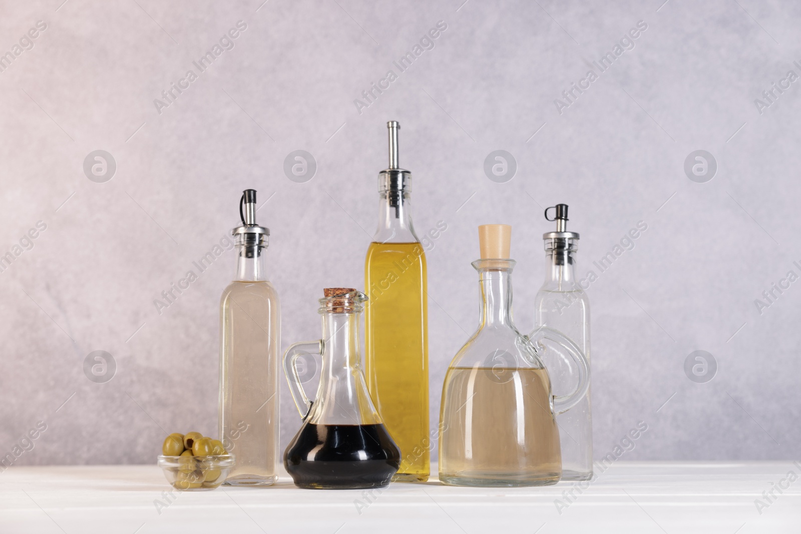 Photo of Bottles of salad dressings and olives on white wooden table