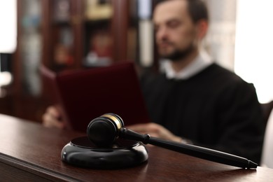 Judge with folder of documents at wooden table in courtroom, focus on gavel