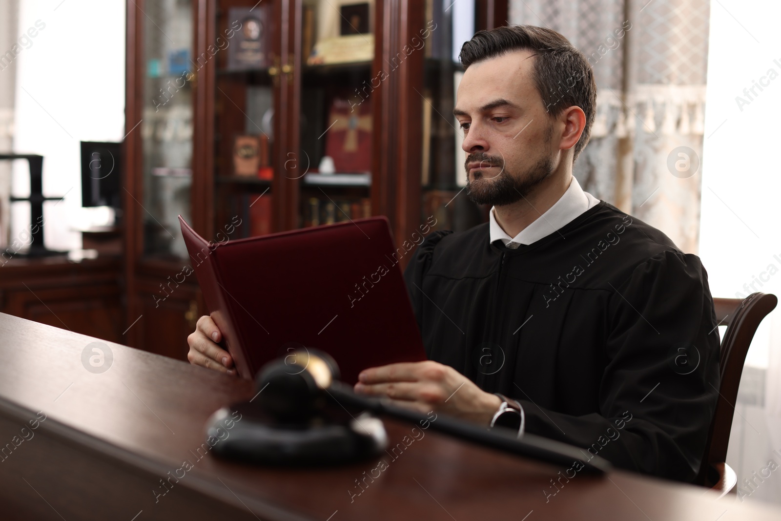 Photo of Judge with folder of documents at wooden table in courtroom