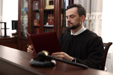 Photo of Judge with folder of documents at wooden table in courtroom