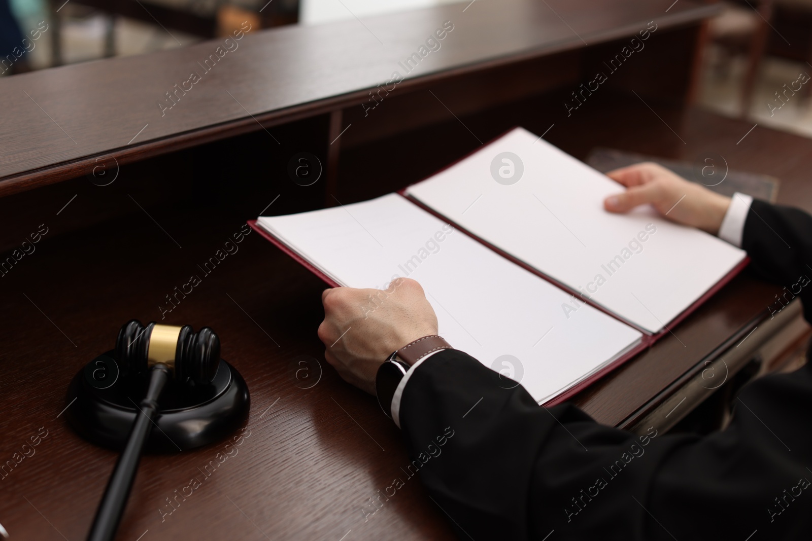 Photo of Judge with folder of documents at wooden table in courtroom, closeup