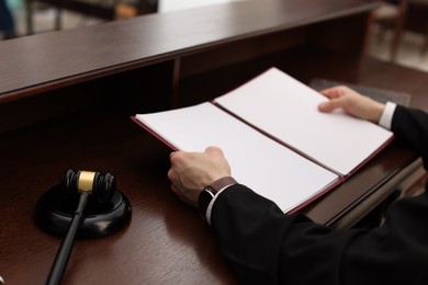 Photo of Judge with folder of documents at wooden table in courtroom, closeup