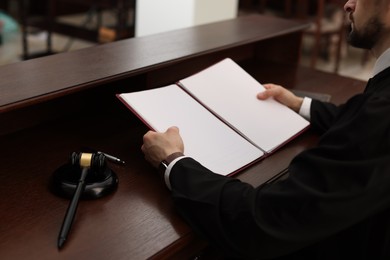 Photo of Judge with folder of documents at wooden table in courtroom, closeup