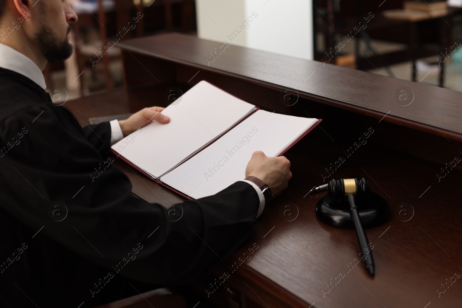 Photo of Judge with folder of documents at wooden table in courtroom, closeup