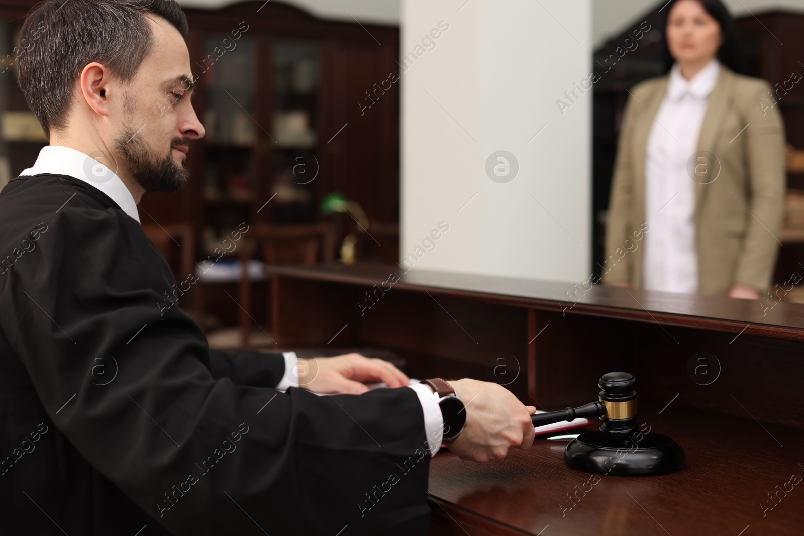 Photo of Judge striking gavel at wooden table in courtroom, selective focus